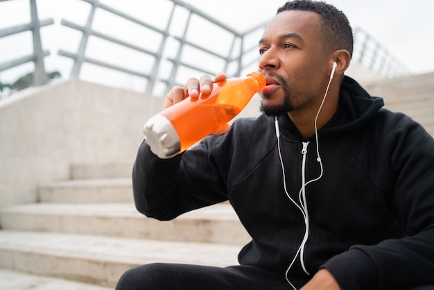 Portrait of an athletic man drinking something after training while sitting on concrete stairs. Sport and health lifestyle.