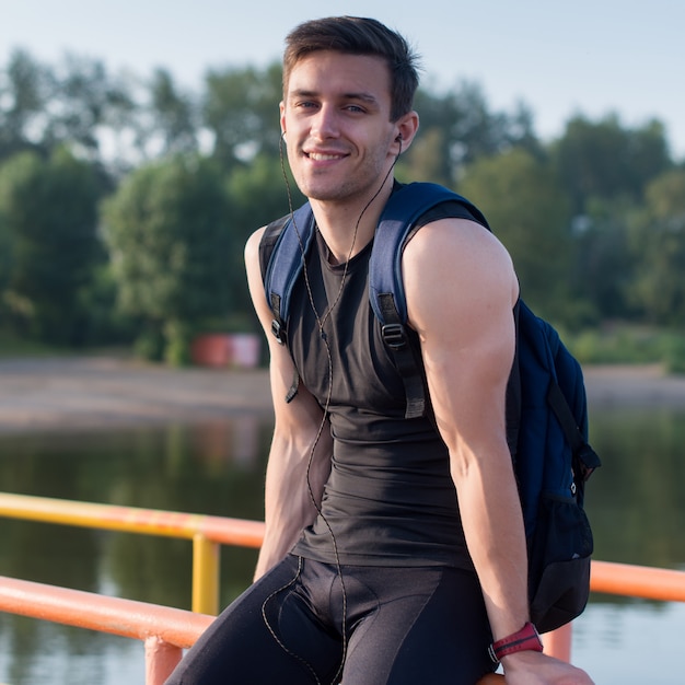 Photo portrait of athletic man sitting on pier near pond