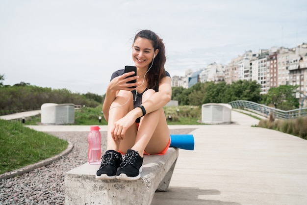 トレーニングの休憩時間に携帯電話を使用している運動女性の肖像画。スポーツと健康のライフスタイル。