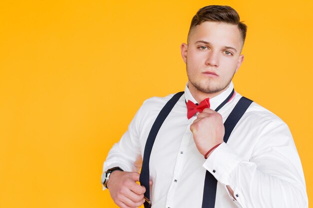 Portrait of an attractive 25 year man businessman hold suspenders on yellow background in ukraine