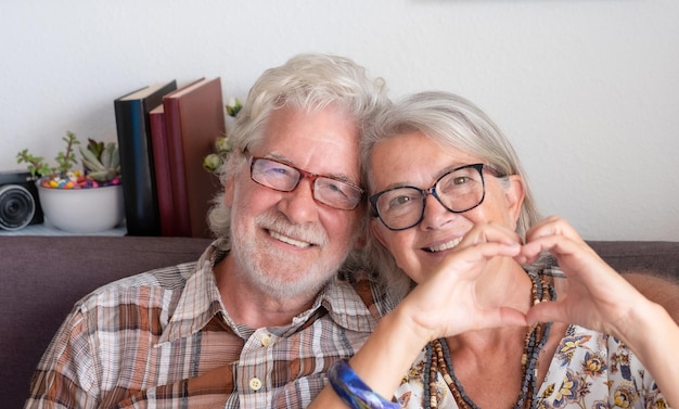 Портрет привлекательной взрослой пожилой пары, делающей сердечный жест пальцами, показывая благодарную любовь
