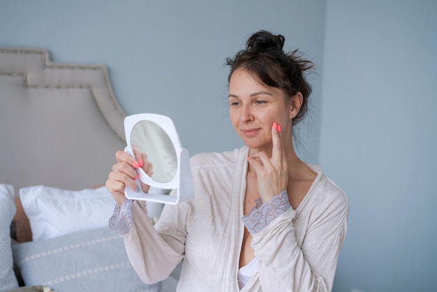 Portrait attractive adult woman applying face cream and holding mirror