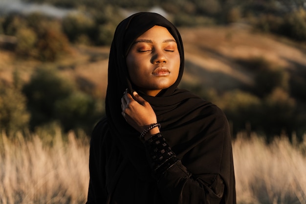 Portrait of attractive african girl in black traditional robe. Salah praying in god.