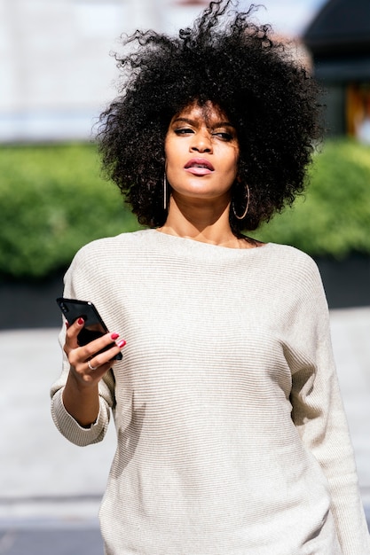 portrait of attractive afro woman using mobile phone in the street. business woman concept