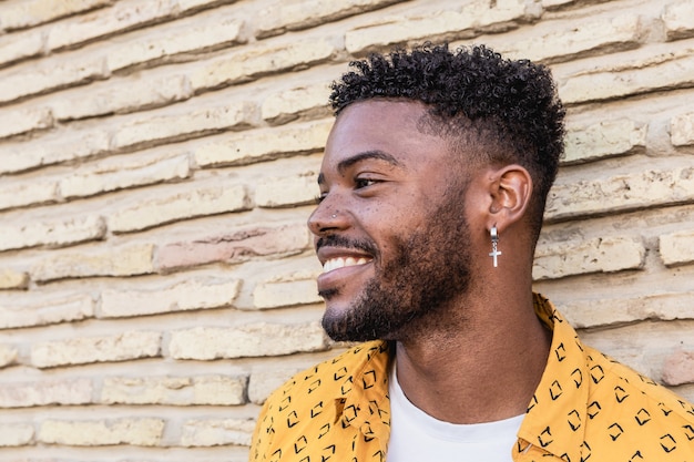 Portrait of an attractive american man with beard and a piercing wearing yellow shirt in a brick wall