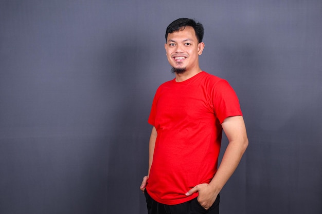 Portrait of attractive asian man in red shirt standing with crossed arm isolated on gray background