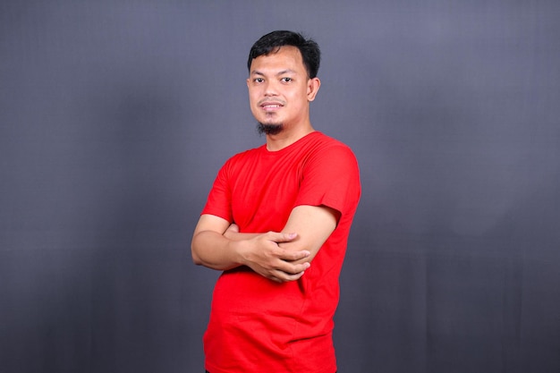 Портрет привлекательного азиатского мужчины в красной футболке, стоящего со скрещенными руками на сером фоне