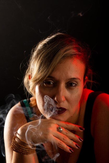 Photo portrait of attractive and beautiful woman with hand on chin incense smoke all around isolated on a black background