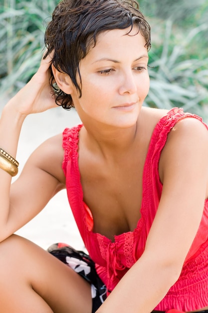 Photo portrait of attractive brunet woman in red sitting on a sand