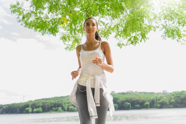 Foto ritratto di donna attraente bruna corridore in esecuzione nel parco cittadino con auricolari fitness sano donna atletica jogging all'aperto natura sfondo sport di motivazione