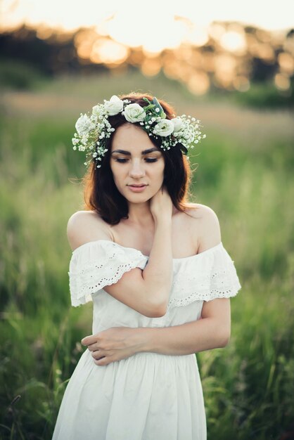 Portrait of attractive brunette girl in white dress and with floral wreath