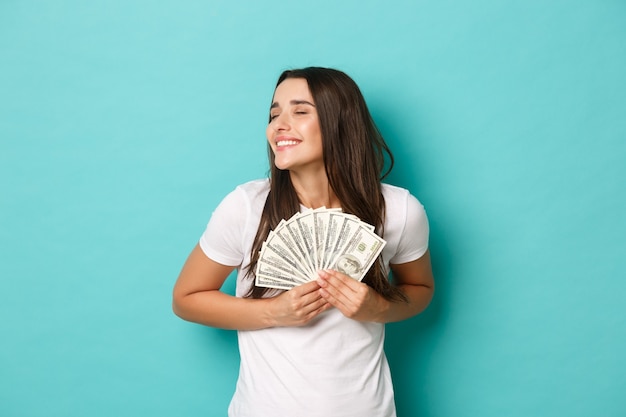 Ritratto di donna attraente bruna in maglietta bianca, sognando di fare shopping, tenendo i soldi