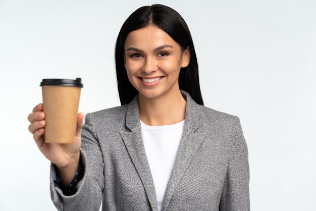 Portrait of attractive business woman holding cupboard mug with coffee and smiling to camera, drink with caffeine, energy boost in morning. Indoor studio shot isolated on white background