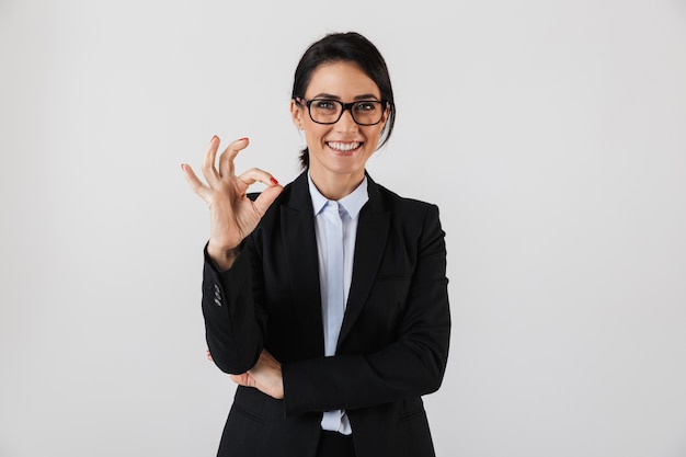 Portrait of attractive businesswoman 30s in formal wear and eyeglasses standing in the office, isolated over white wall