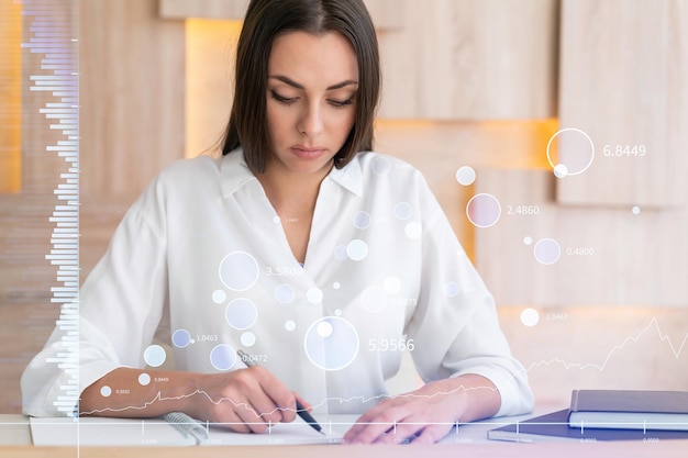 Portrait of attractive businesswoman in formal wear working with documents and thinking how to optimize trading strategy at corporate finance fund Forex chart hologram over modern office background