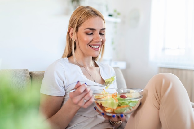 Ritratto della donna sorridente caucasica attraente che mangia insalata. donna che mangia insalata sana con pomodori ciliegia in casa stile di vita sano