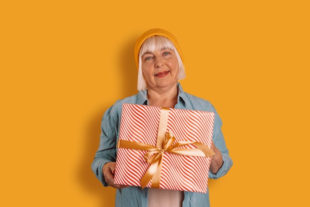 Portrait of attractive cheerful funny 50s woman holding in hands gift good mood isolated over bright orange color background