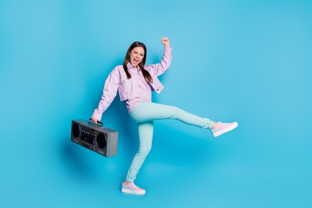 Portrait of attractive cheerful girl carry music player dancing isolated on blue background