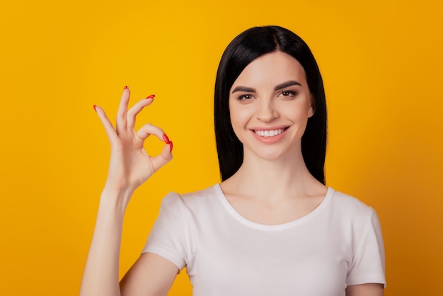 Portrait of attractive cheerful girl showing ok-sign ad solution isolated over bright yellow color background