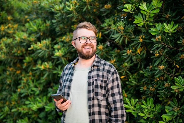 Ritratto di attraente ragazzo allegro che utilizza lo smartphone per scorrere sui social media su sfondo verde albero copia spazio e posto vuoto per il testo