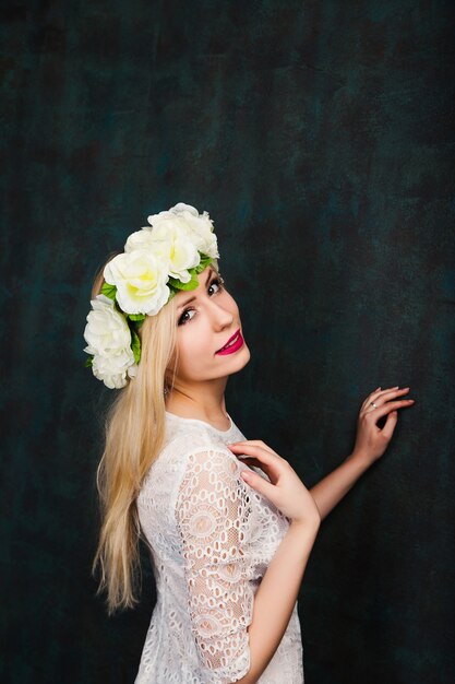 Portrait of attractive cheerful young woman in white dress and flower wreath