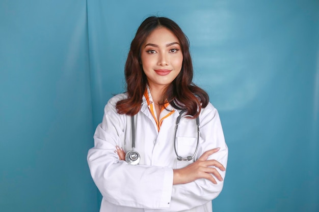 Portrait of an attractive confident female doctor friendly smiling arms crossed wear white lab coat stethoscope isolated blue color background