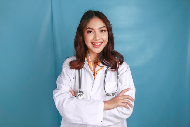 Portrait of an attractive confident female doctor friendly smiling arms crossed wear white lab coat stethoscope isolated blue color background