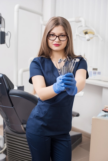 Portrait of attractive female dentist holding dental tools at the modern dental office. Dentistry