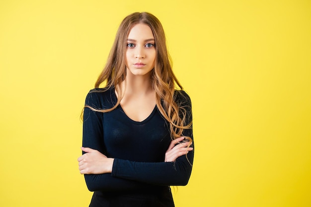 Photo portrait of attractive female teenager model with long hair in black sexy dress posing on yellow background in studio