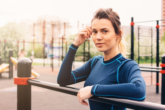 Portrait of attractive fit young woman in sport wear rest on the street workout area. 