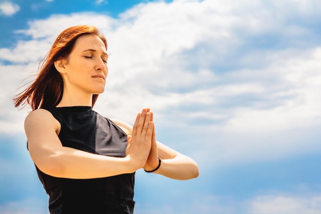 Foto ritratto di donna attraente fitness rilassante posizione yoga contro lo sfondo del cielo.