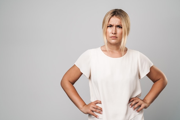 Portrait of an attractive frowning confused woman standing isolated over gray wall