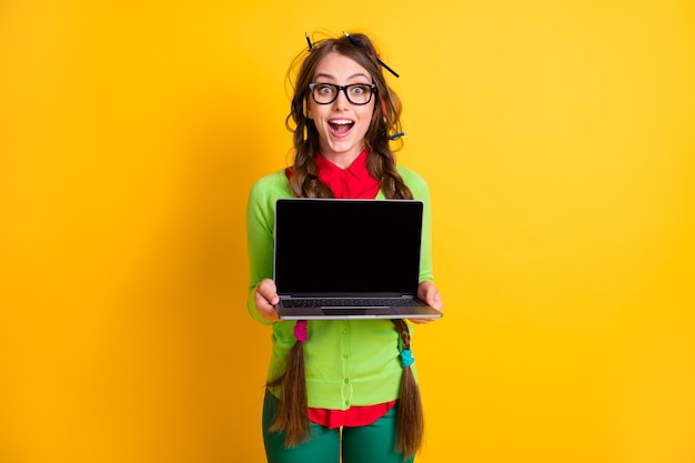 Photo portrait of attractive funky cheerful girl holding in hands demonstrating laptop screen remote job isolated shine yellow color background