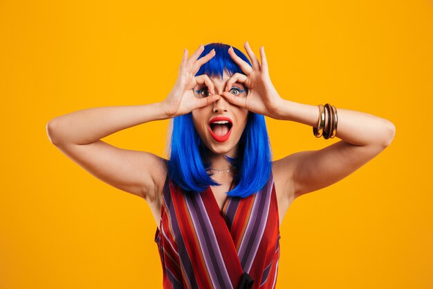 Foto ritratto di un'attraente ragazza funky con i capelli blu che indossa un abito casual in piedi isolata sul muro giallo, mostrando un gesto ok