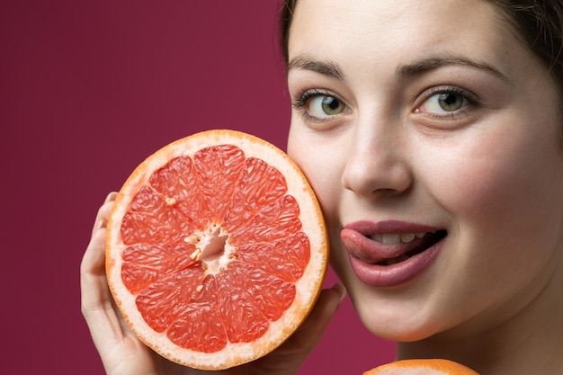 Portrait of an attractive girl holding a sliced Ã¢ÂÂÃ¢ÂÂslice of grapefruit on a red background.