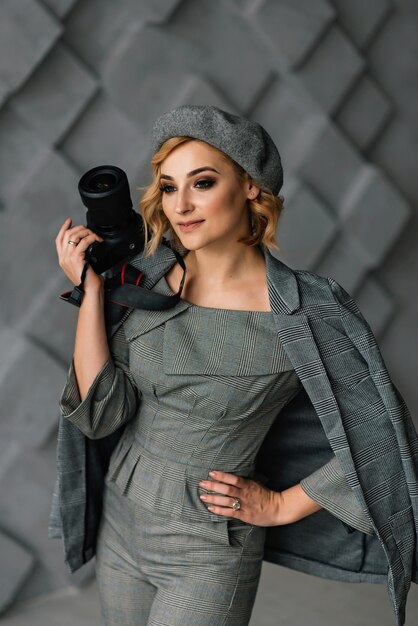 Portrait of an attractive girl photographer in stylish clothes and a beret with a camera in her hands. The concept of creative professions.