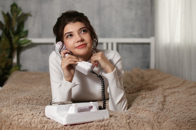 Ritratto di ragazza attraente utilizzando il telefono in mano vicino all'orecchio sdraiato sullo stomaco parlando con l'amante divertendosi