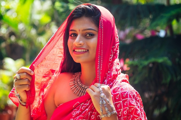 Портрет привлекательной индийской женской модели в отпуске на райском тропическом пляже океанским морем. индуистская женщина с набором украшений кундан традиционный индийский костюм красная свадьба сари. азиатская девушка чувственный взгляд
