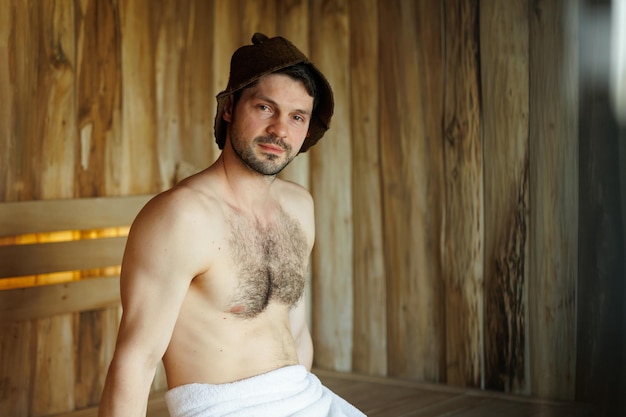 Portrait of a attractive man sitting in a wooden sauna during a spa treatment in a hotel