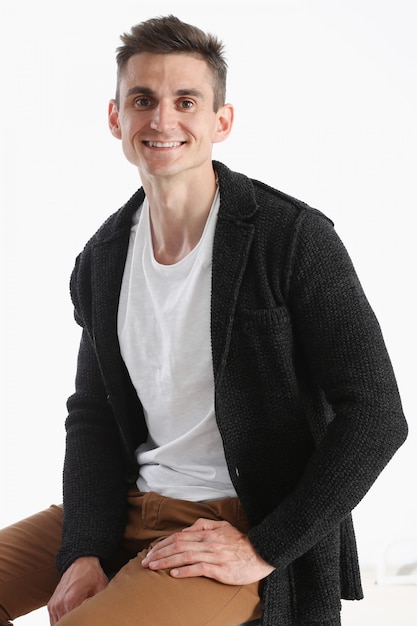 Portrait of an attractive man in a sweater and a T-shirt, sitting on a chair and smiling