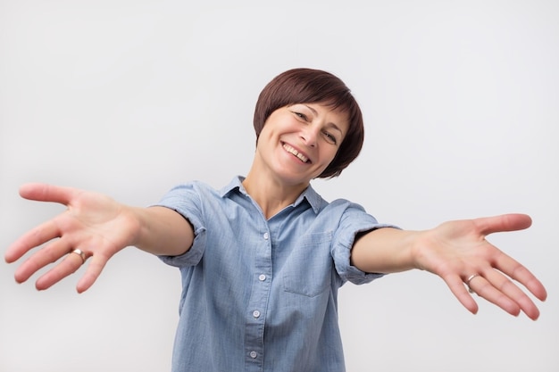 Portrait of attractive mature woman raised up arms hands at you She is dressed in blue shirt