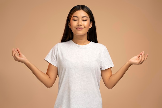 Portrait of attractive peaceful young woman relaxing and doing meditation gesture