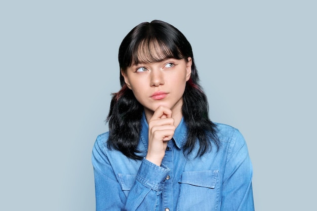 Portrait of attractive pensive young female touching her chin with hand looking away creating solution copy space on light gray color isolated background Question doubt curiosity reflection choice