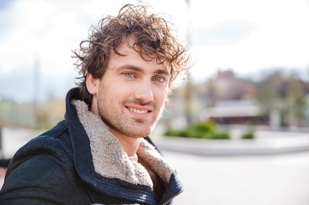 Portrait of attractive positive smiling happy curly young man in black jacket