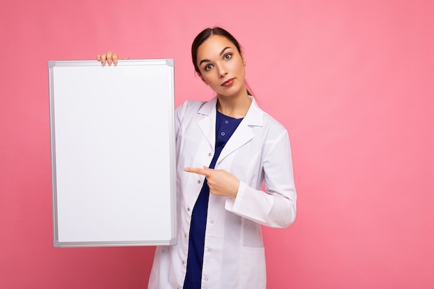 Portrait of attractive pretty young positive brunette woman wearing medical white coat holding white