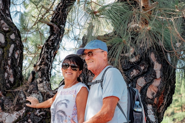 Portrait of attractive senior couple walking in the forest during a mountain excursion looking at camera smiling