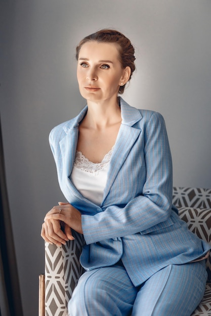 파란색 정장을 입고 안락의자에 앉아 포즈를 취하는 매력적인 진지한 여성의 초상화. 성공적인 여성의 개념
