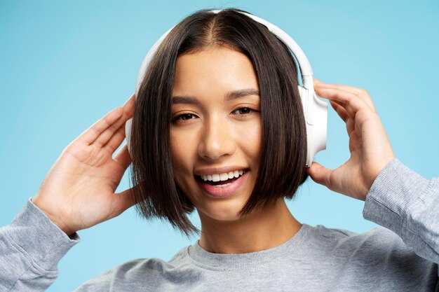 Foto ritratto di un'attrattiva donna asiatica sorridente che indossa le cuffie e ascolta musica guardando la telecamera isolata sullo sfondo blu in primo piano