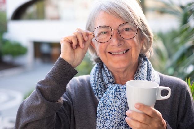 Portrait of attractive smiling senior woman with eyeglasses drinking hot coffee or tea