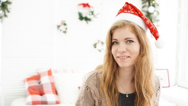 nomeでクリスマス帽子の魅力的な笑顔の女性の肖像画-明るく居心地の良い部屋